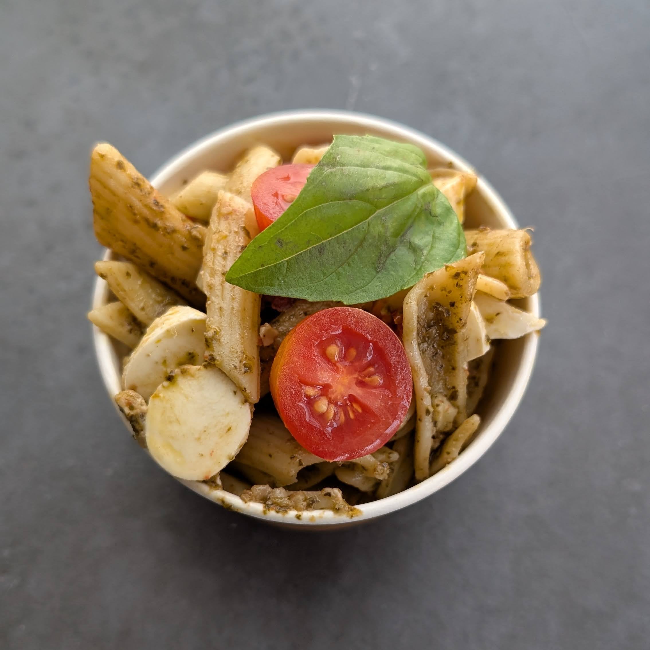 Pasta dish with tomatoes and basil in a white bowl on a dark surface
